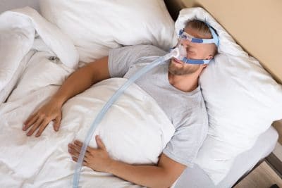 young adult man sleeping with a bulky cpap mask on