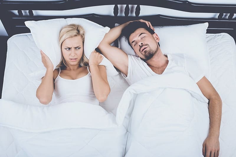 Woman using pillow to cover her ears while partner snores