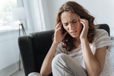 woman sitting in her living room with a migraine headache