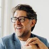 services-cosmetic-min Smiling man in glasses, highlighting the results of cosmetic dentistry with bright, well-aligned teeth.