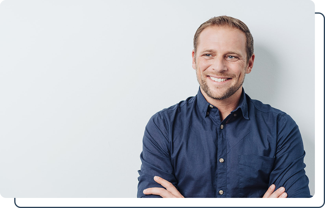 Smiling man in a navy blue shirt standing against a plain white background with arms crossed.